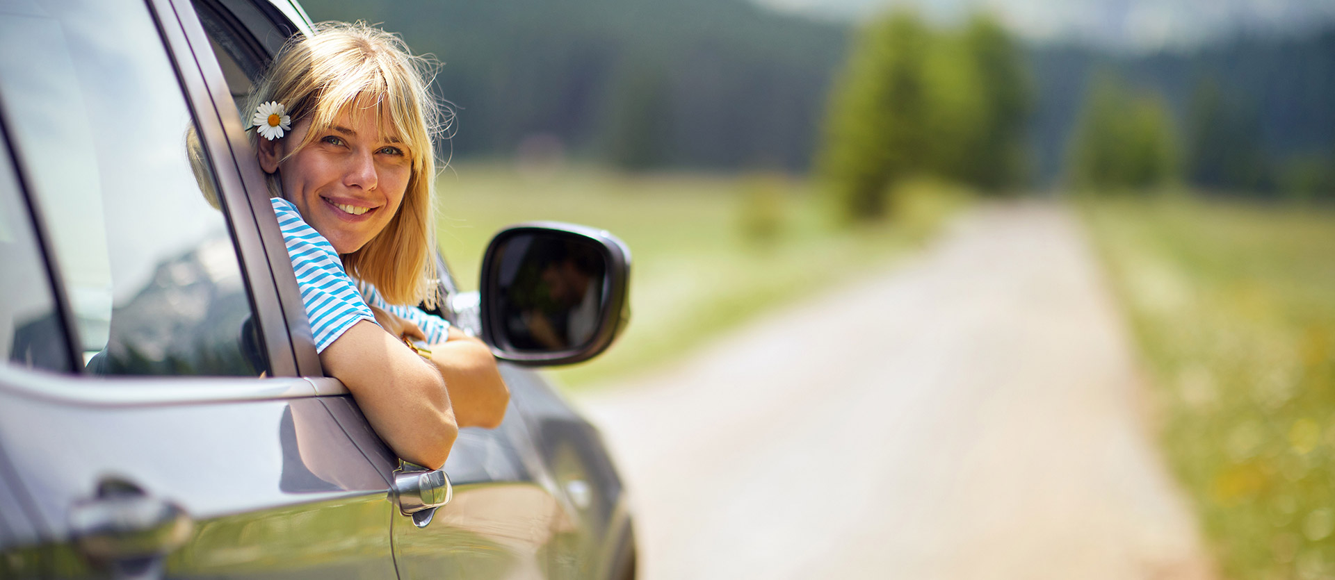 Woman hanging out of her car smiling with a flower in her hair. 
