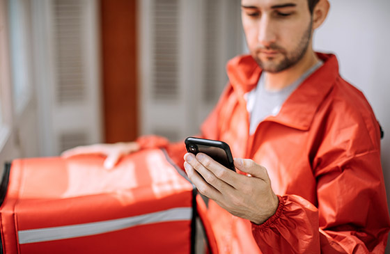 Man looking at his phone while delivering pizzas. 