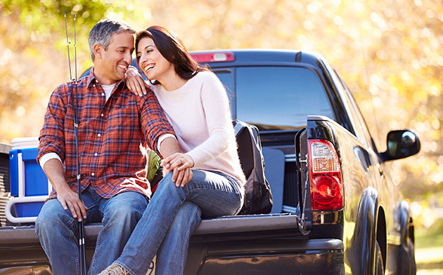 Man and woman sit on the bed of their truck. 